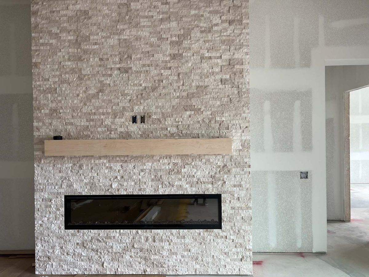 Stacked stone fireplace wall with a linear fireplace and a wood mantel