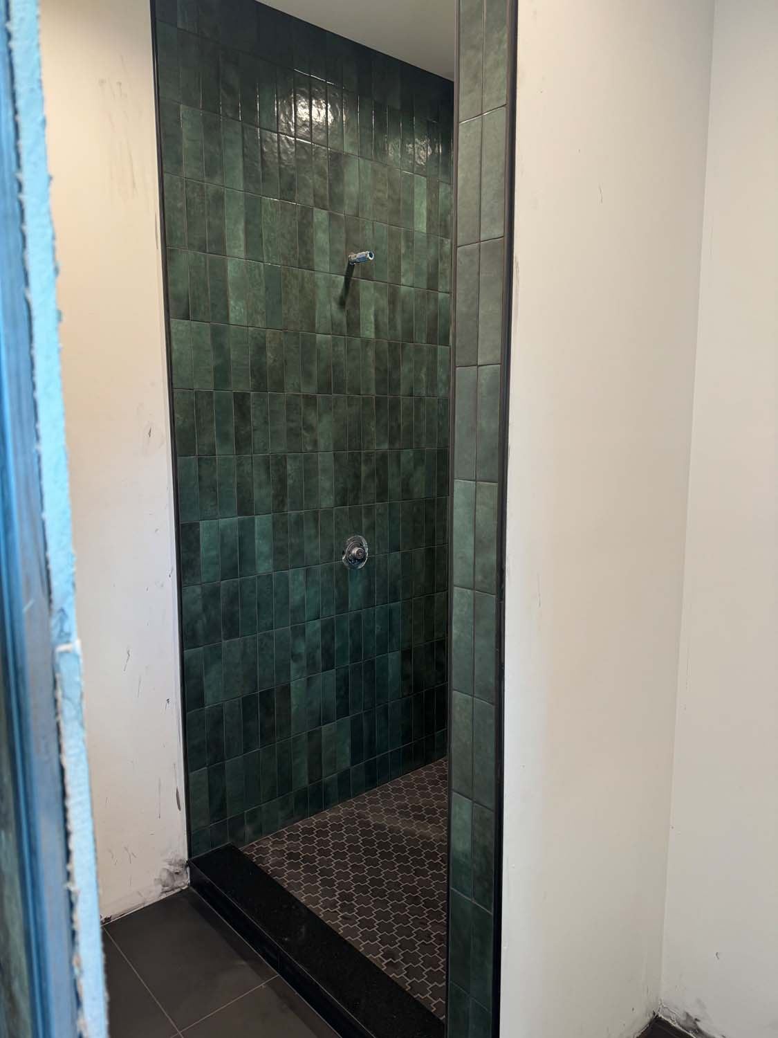 Green glazed vertical tile shower with a dark mosaic floor