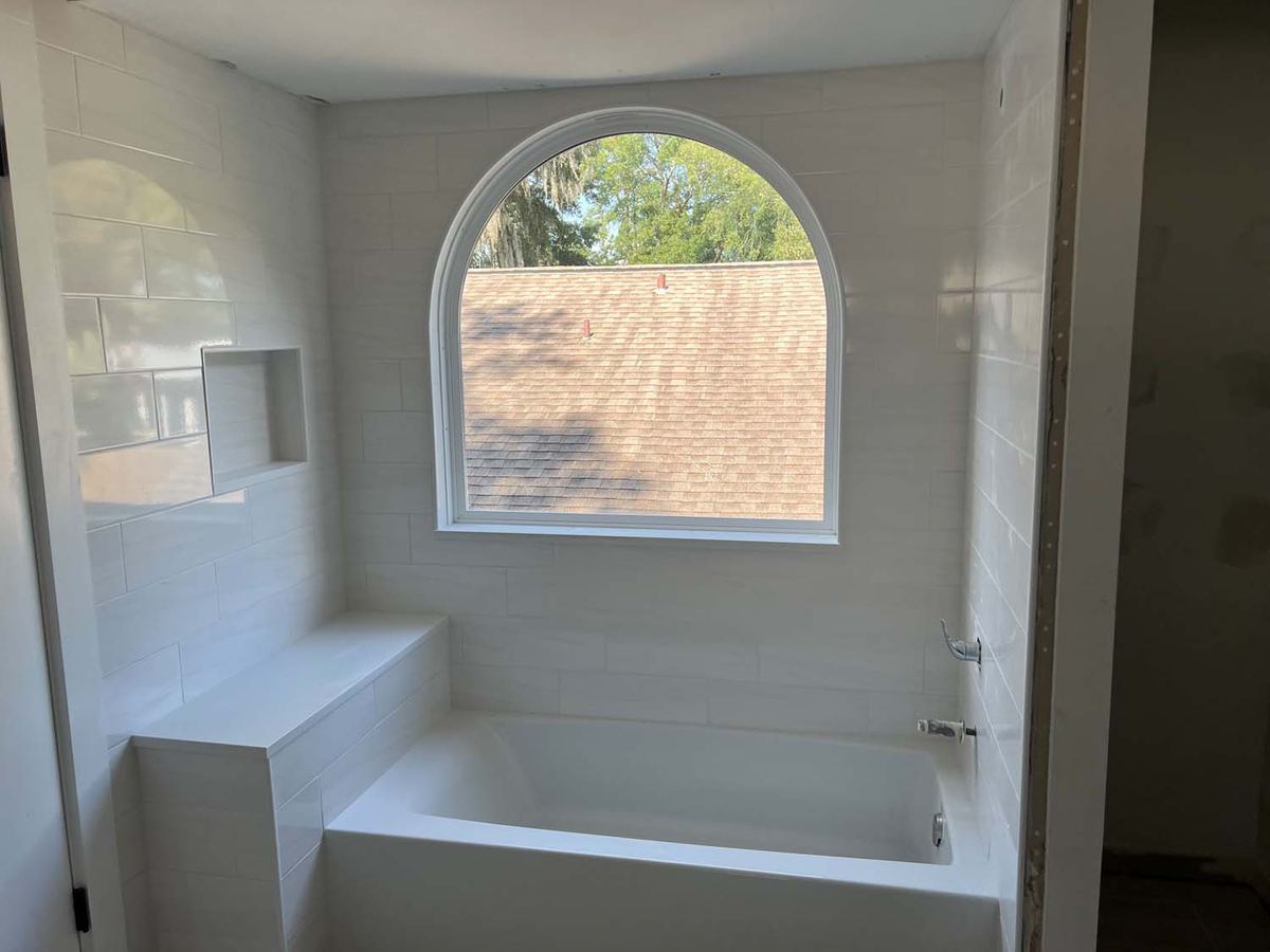 Soaking tub surround in large white tile under an arched window