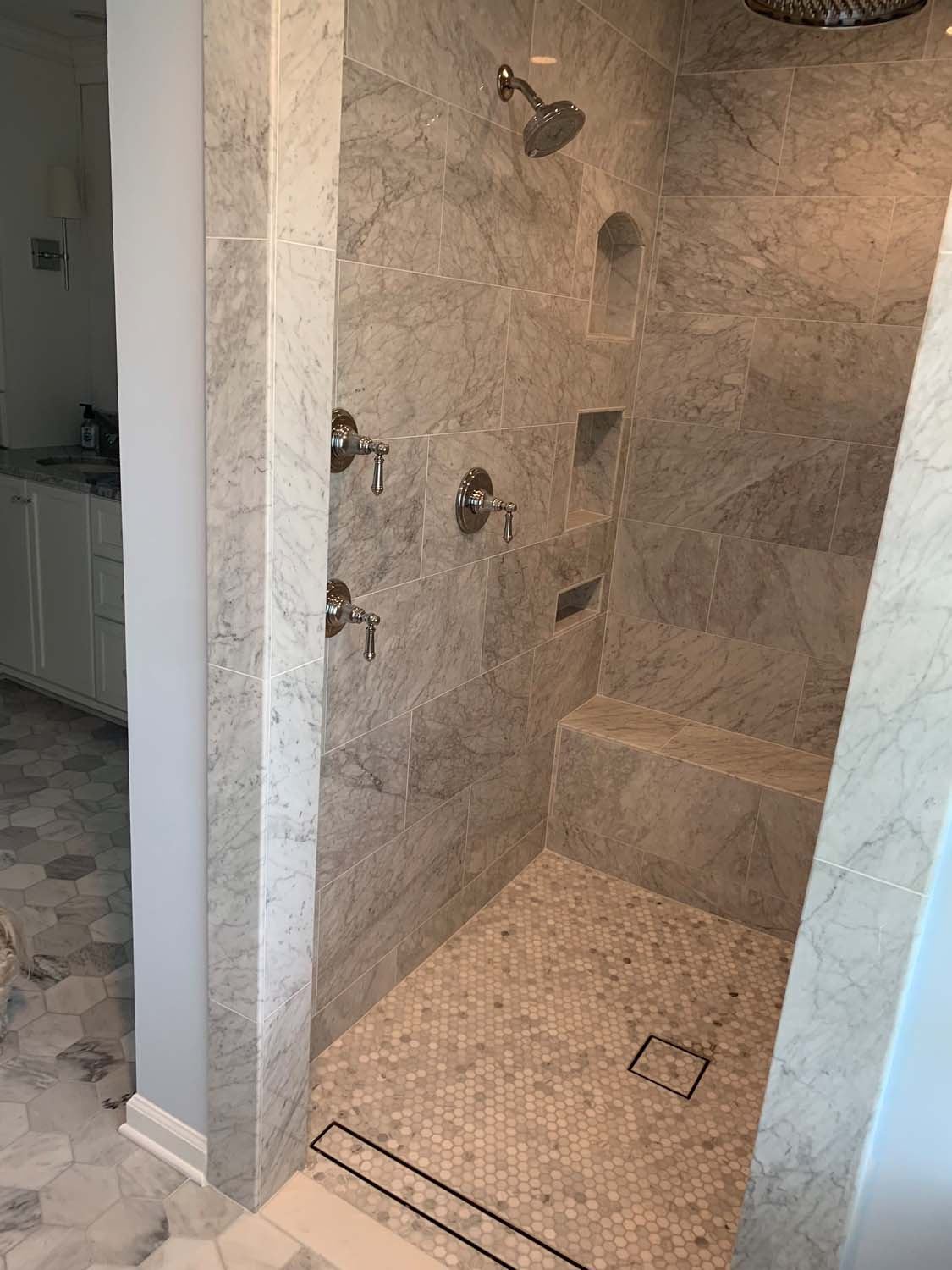 Marble-look walk-in shower with a bench and a mosaic floor