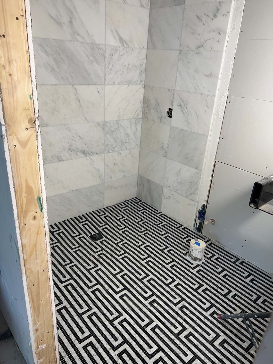 Marble-look shower walls over a black and white geometric floor