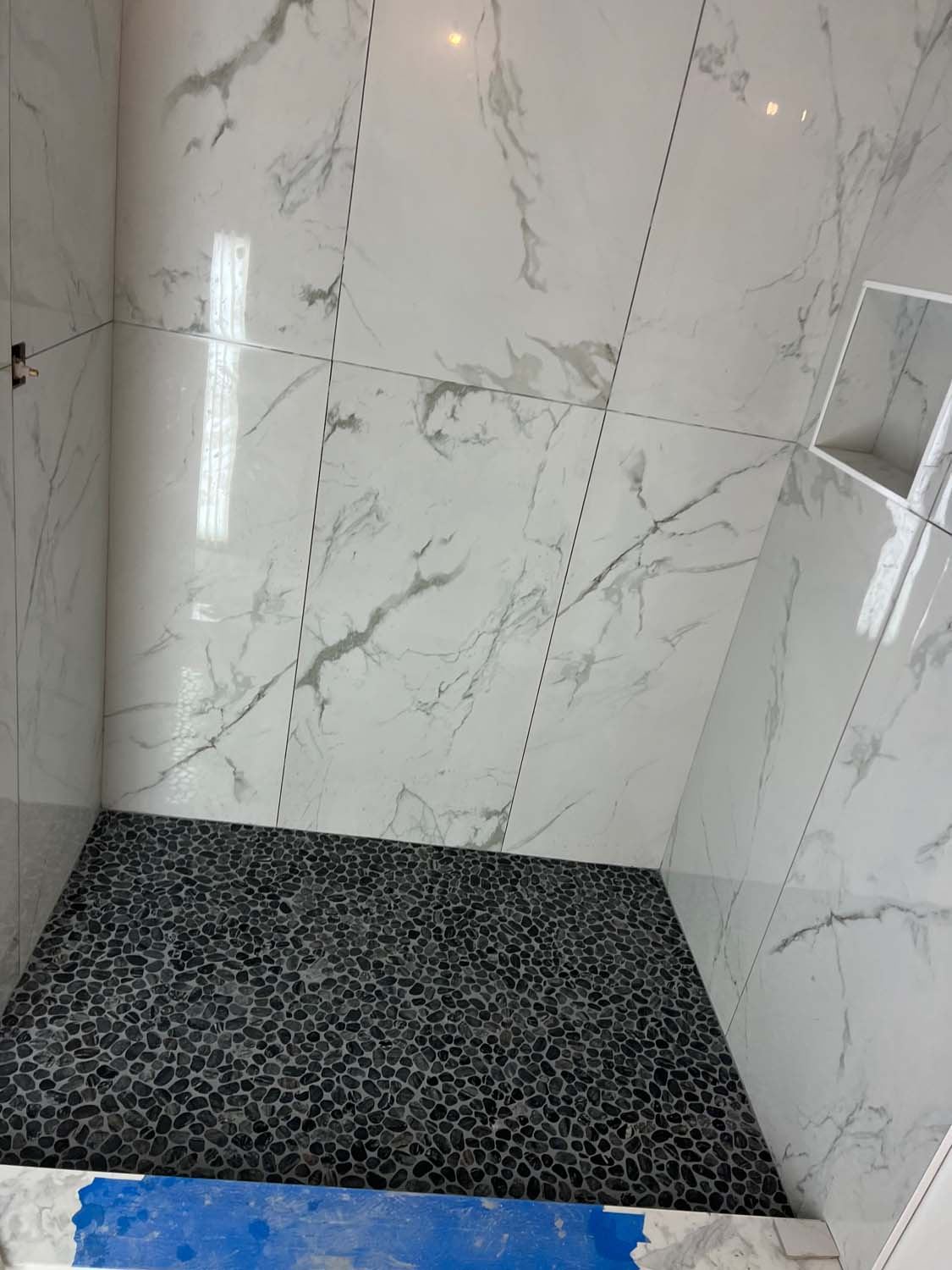 Calacatta-look shower walls with a black pebble floor