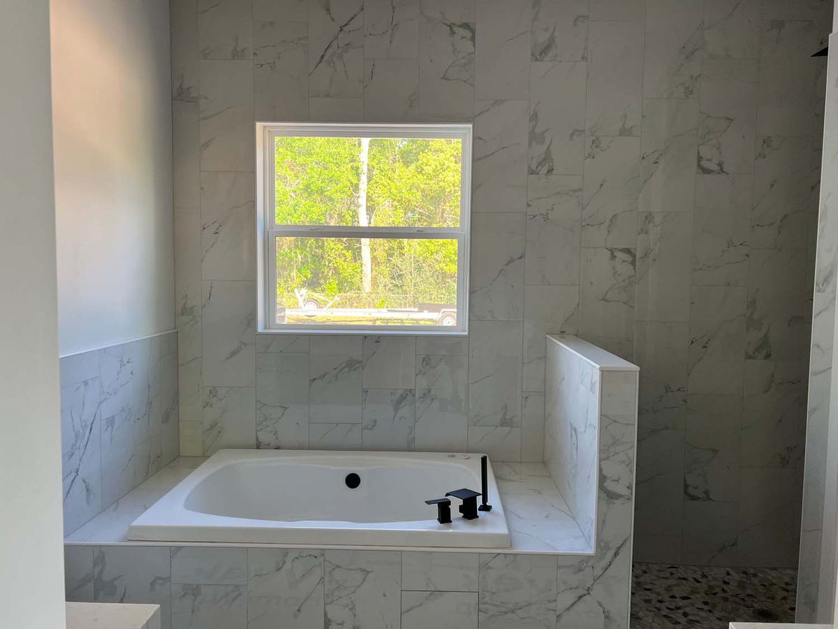 Drop-in tub with a marble-look tile surround under a window