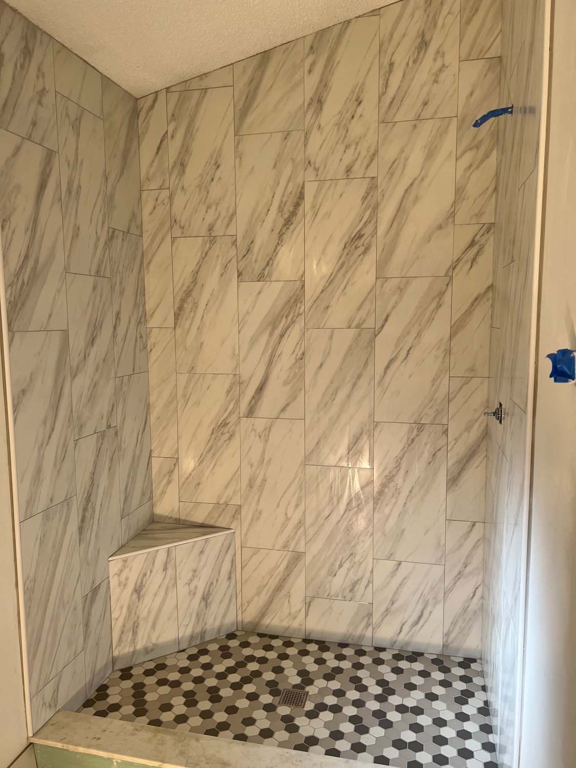 Marble-look shower with a corner bench and a hexagon floor
