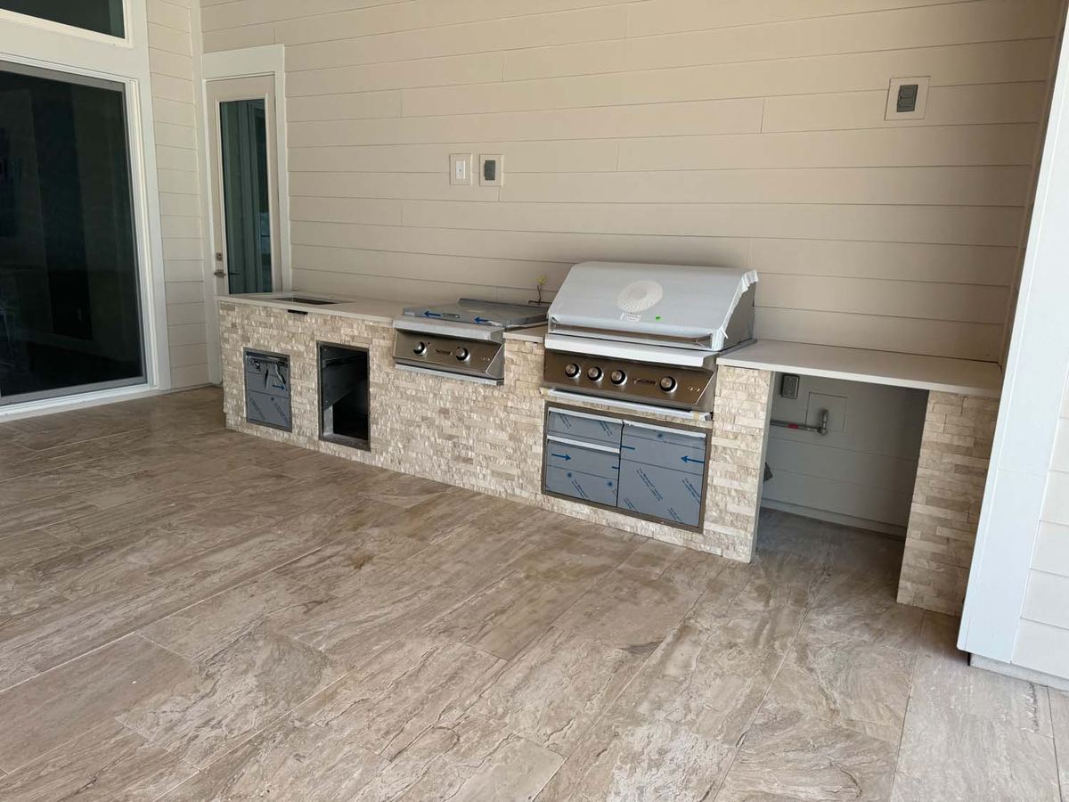 Outdoor kitchen with a stacked stone island and grill on a porcelain floor