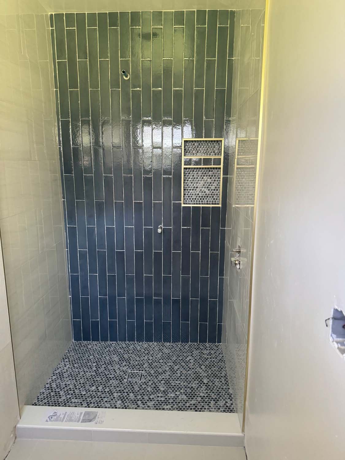 Deep green vertical tile shower with a lit niche and a pebble floor