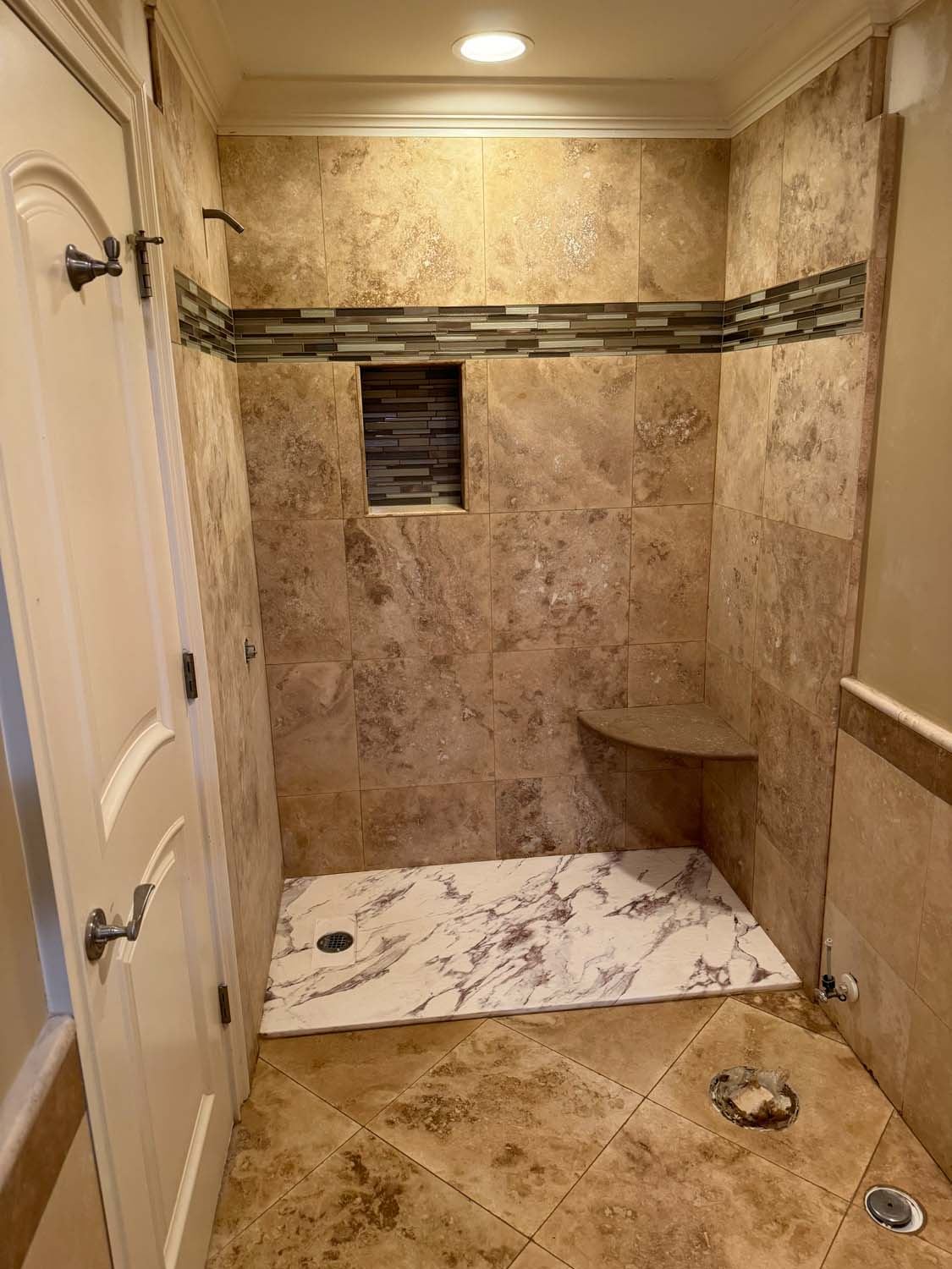 Travertine shower with a glass mosaic band and a corner bench