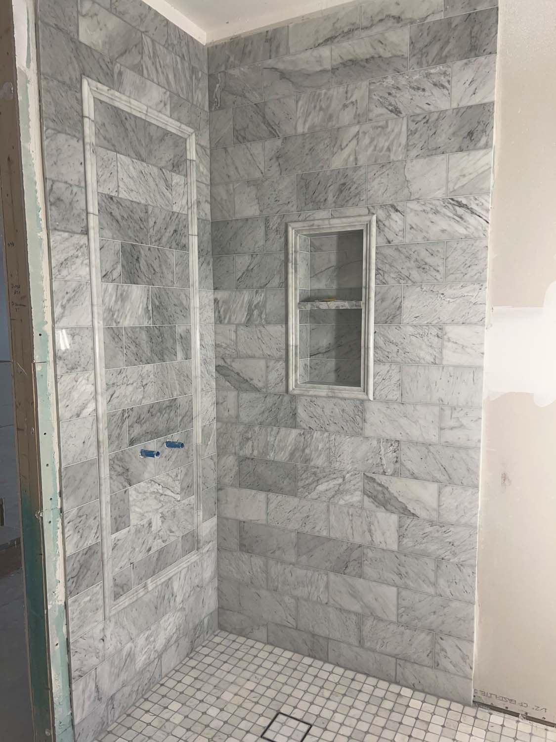 Gray marble shower with a framed niche and a mosaic floor