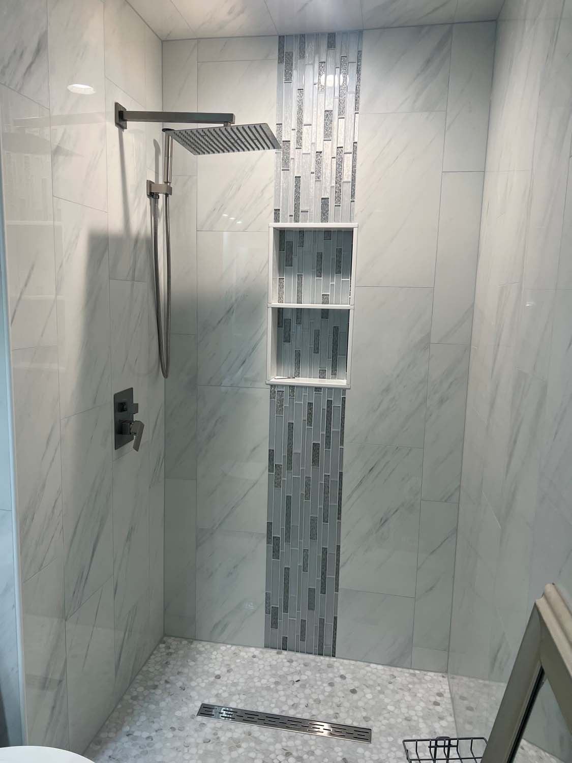 Marble-look shower with a vertical mosaic stripe, three niches and a linear drain