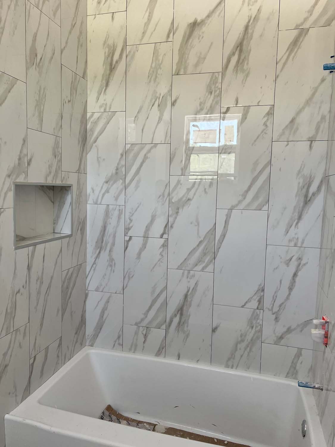 Marble-look tile around a soaking tub under a window