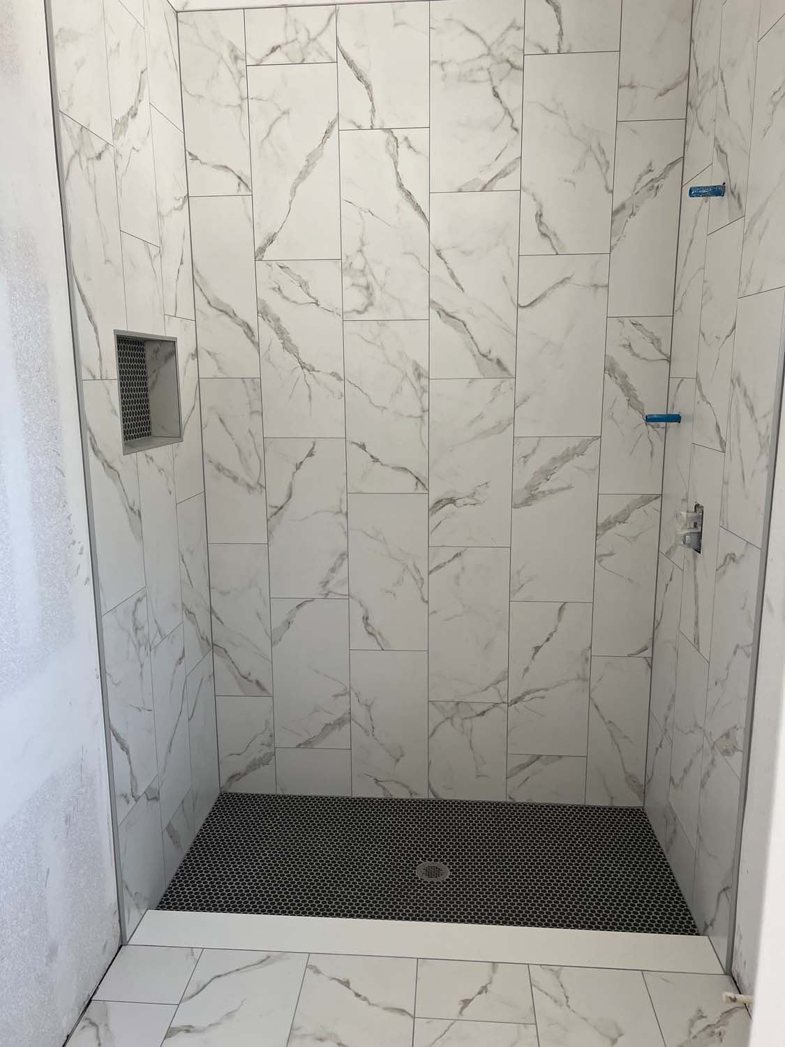 Marble-look shower with a black mosaic floor and a niche