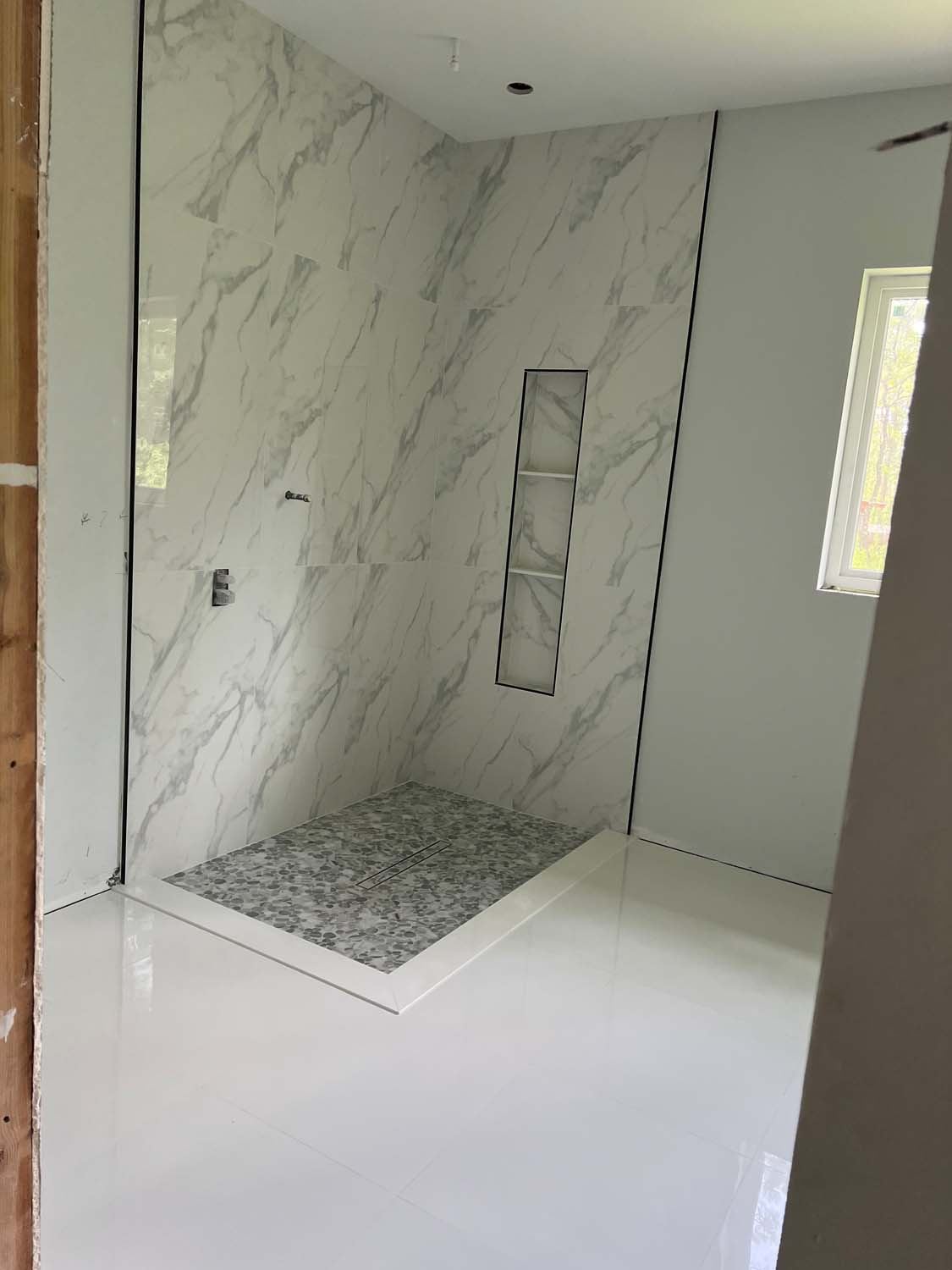 Marble-look shower with a tall niche and a mosaic floor