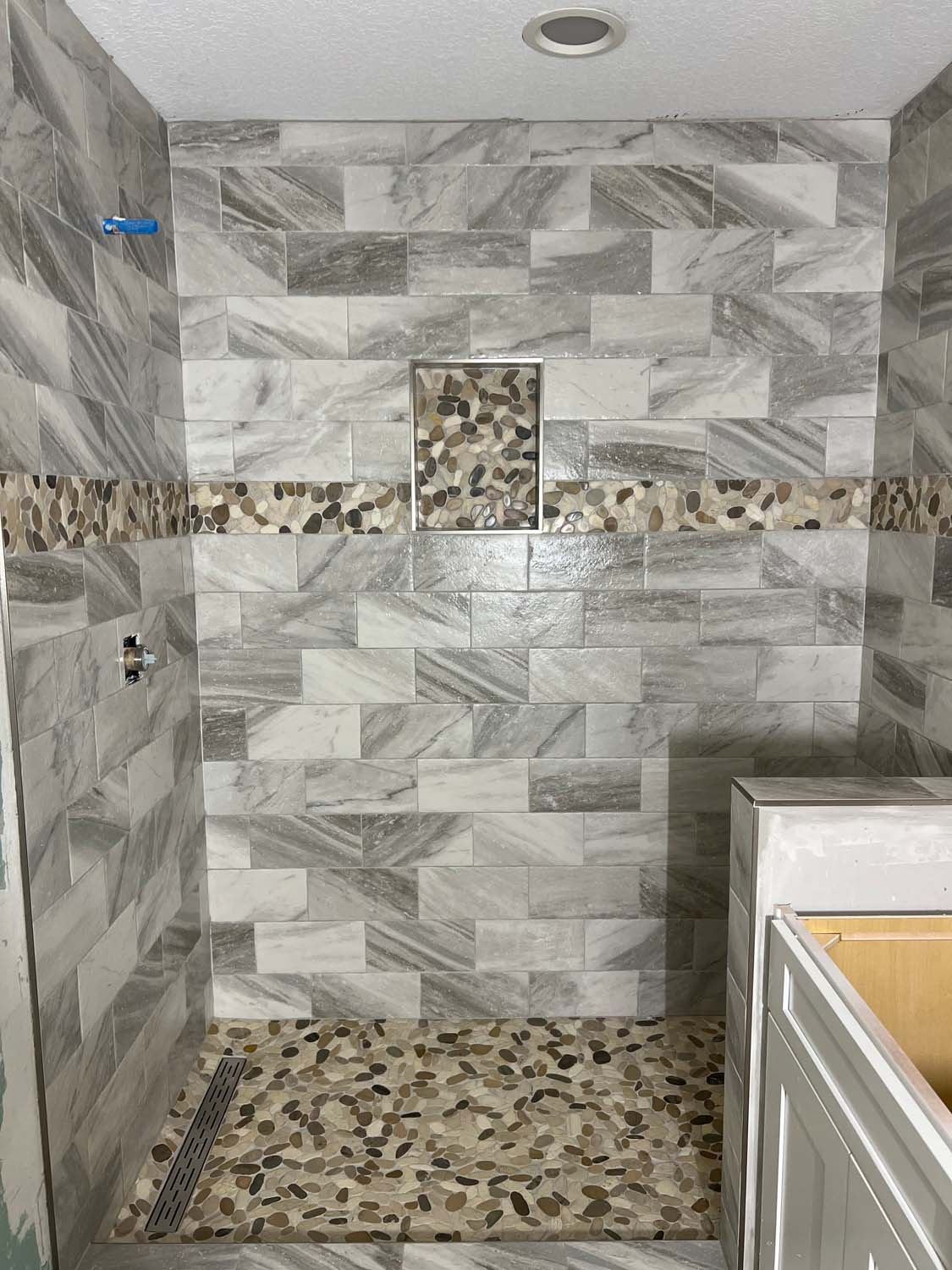 Gray marble shower with a pebble accent band and floor