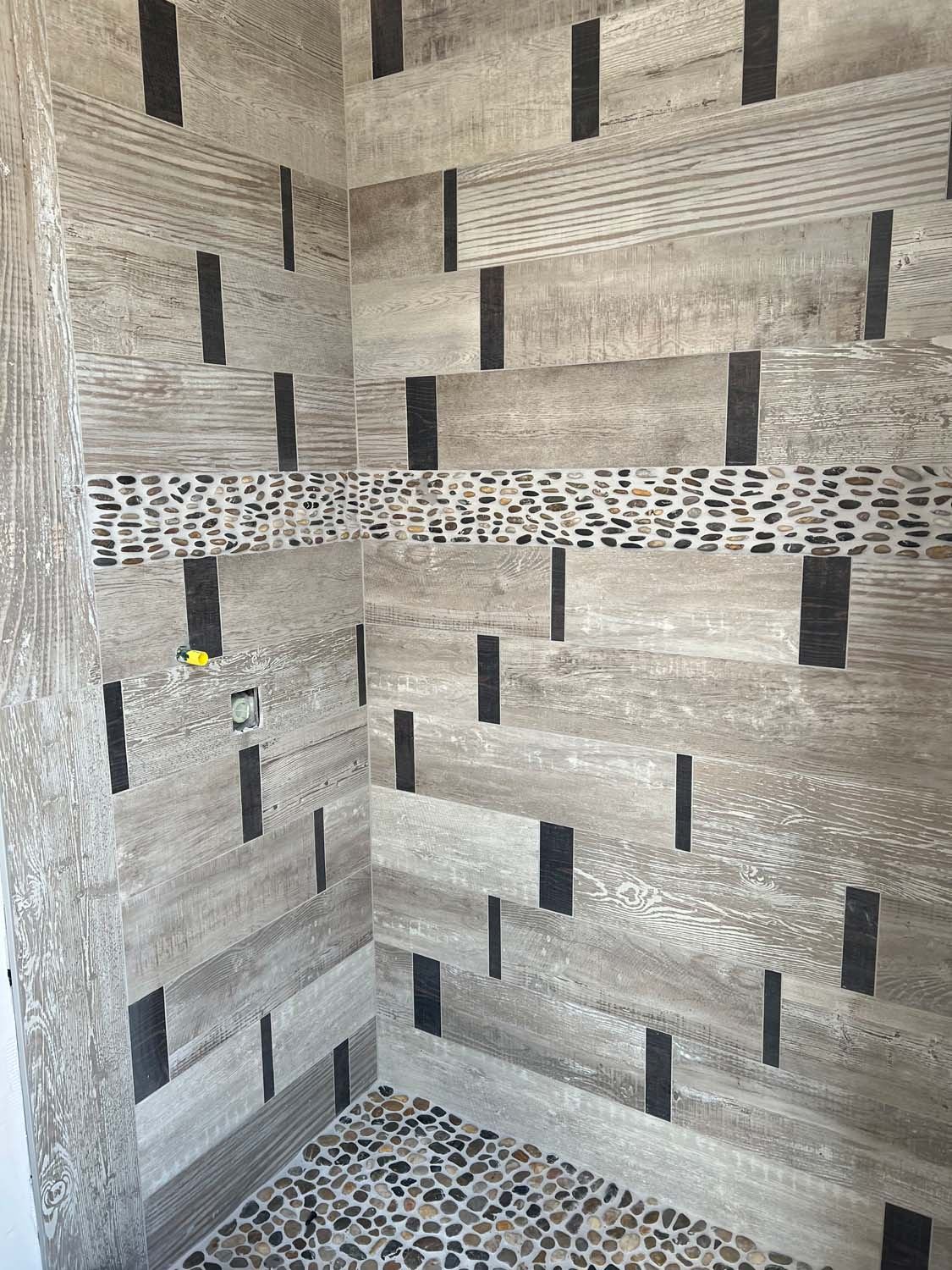 Wood-look shower with a pebble band and black accent tiles