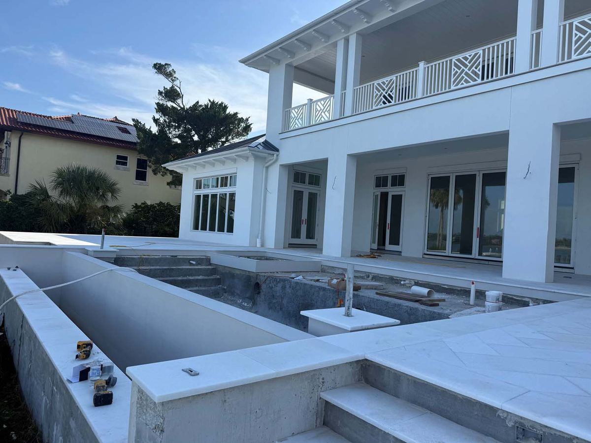 Pool coping and deck in white stone at a two-story home