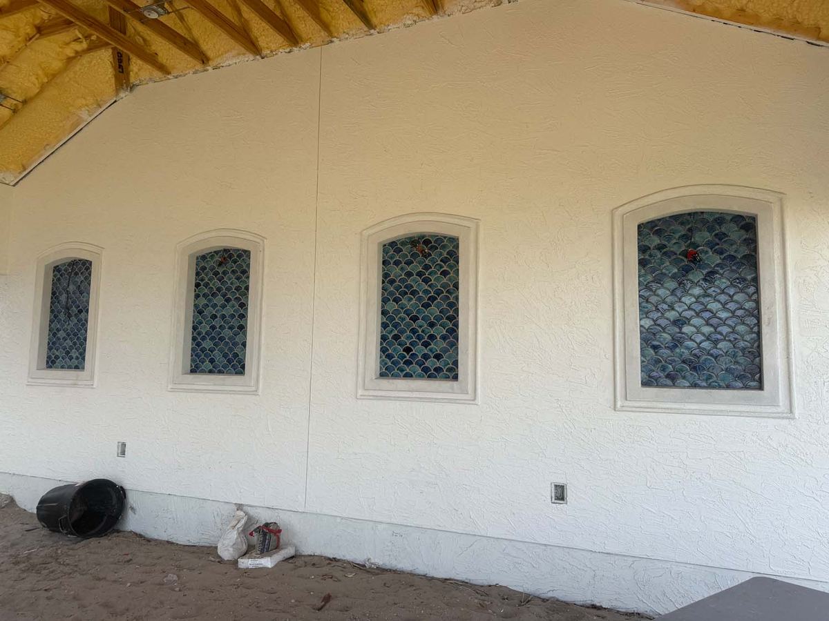 Mosaic tile insets in arched window recesses on a stucco wall