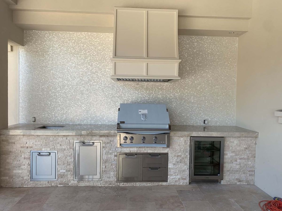 Outdoor kitchen with an iridescent mosaic backsplash and a stone veneer island